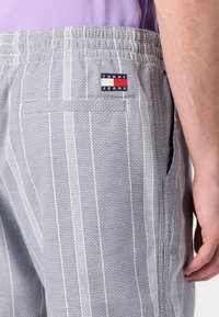 Graue gestreifte Shorts aus strukturiertem Stoff, mit elastischem Bund, seitlichen Taschen und einem Tommy Jeans Logo-Patch auf der Rückseite.