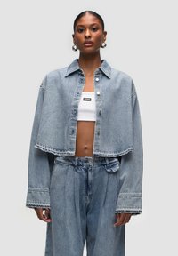 Giacca di jeans croppata in blu chiaro con chiusura a bottoni e bordi grezzi. Abbinata a pantaloni di jeans a vita alta con vestibilità rilassata.