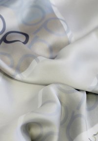 Tela de seda en gris claro con patrones circulares en azul y beige, exhibiendo una textura suave y pliegues suaves.