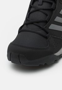 Czarny but sportowy z teksturowanym syntetycznym cholewkami, wzmocnioną noskiem i gumową podeszwą z bieżnikiem. Zawiera odblaskowe akcenty.