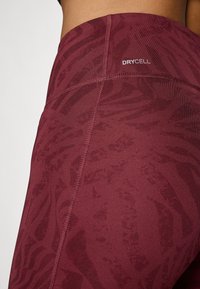 Maroon leggings with a textured pattern, featuring a high waistband and visible seams. "DRYCELL" logo on the side for moisture management.