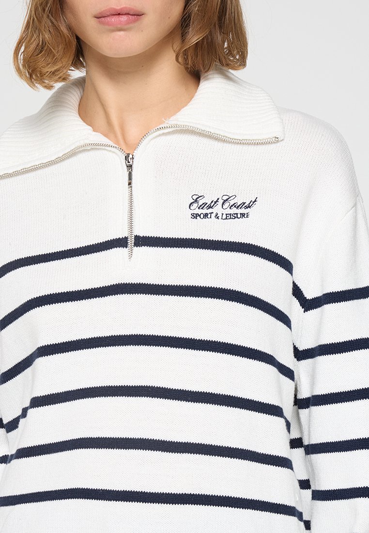 Suéter blanco de punto con rayas azul marino, cuenta con un cuello con cremallera y el bordado "East Coast SPORT & LEISURE" en el pecho.
