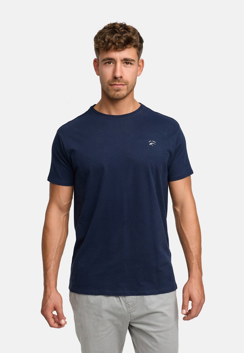 Granatowa bawełniana koszulka z krótkim rękawem i okrągłym dekoltem. Posiada małe białe logo na piersi. Gładka tekstura.