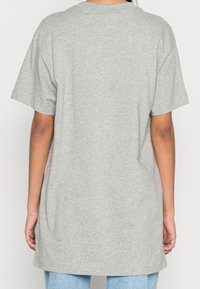 Camiseta de algodón gris con cuello redondo y mangas cortas, que presenta un corte relajado y un dobladillo trasero ligeramente alargado. Textura suave y lisa.