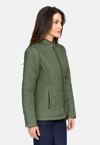 Chaqueta verde acolchada con cuello alto, que presenta patrones en diagonal y de tejido de cesto, cremallera frontal y bolsillos laterales. Textura suave.
