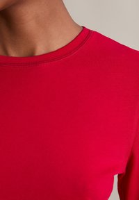 Czerwona bawełniana koszulka z okrągłym dekoltem. Gładka tekstura i dopasowany krój, z wyraźnym przeszyciem wzdłuż dekoltu.