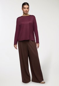 Maglietta lunga bordeaux con vestibilità ampia, abbinata a pantaloni beige a gamba larga. Tessuto morbido e liscio con una leggera lucentezza e scollatura rotonda.