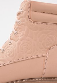 Ljust rosa stövel med präglade blommönster, sydda detaljer och rosa snören trätt genom metalldragkedjor.