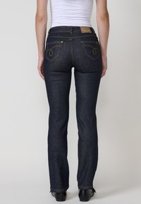 Temno modri jeans s ravnimi hlačnicami, ki imajo rumeno šivanje in dva zadnja žepa z okrasnimi vzorci.