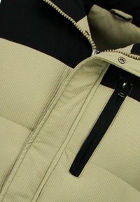 Groen-zwart geïsoleerd jack met een doorgestikt ontwerp, voorzien van een ritszak en een gestructureerde stof. Horizontaal geribd patroon op de stof.