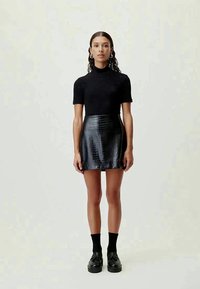 Black short-sleeve turtleneck top paired with a black faux crocodile-skin mini skirt. Model wears black socks and chunky black shoes.