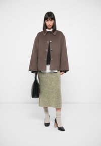 Brown wool-blend coat with a round collar and button closure, layered over a black sweater and striped shirt. Green skirt, black bag, and heels.