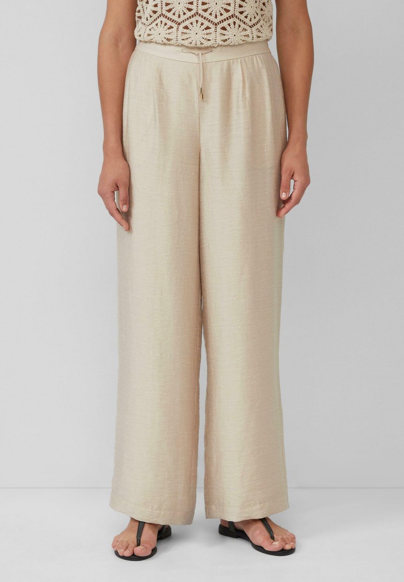 Beige Weitbeine-Hosen mit strukturiertem Finish, ausgestattet mit einem elastischen Taillenbund und Kordelzug, kombiniert mit flachen schwarzen Sandalen.