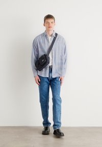Camicia a righe con bottoni, t-shirt bianca, jeans blu strappati, borsa a tracolla nera e scarpe nere. Stile minimalista con vestibilità dritta.