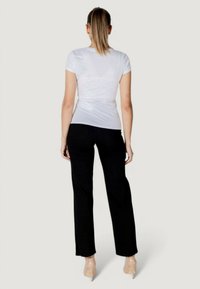 Camicia bianca a maniche corte con un design aderente, abbinata a pantaloni neri a gamba dritta. L'outfit è completato da scarpe col tacco trasparente.