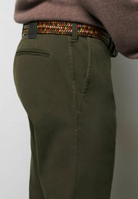 Olijfgroene broek met een gestructureerde afwerking, voorzien van een geweven riem in rood, groen en goudtinten. Inclusief zijzak en detail van een achterzak.