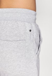 Gray sweatpants with a soft texture, featuring a wide waistband, side pockets, and a small black logo near the pocket.