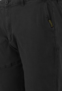 Svarta bomullsshorts med en slät yta, med ett framknäppning och en sidoficka. En gul logotag syns på sidan.