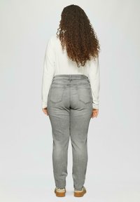 Graue High-Waist-Jeans mit einer engen Silhouette, fünf Taschen und dezenten Steppnähten. Tragen zu einem weißen Langarmshirt.