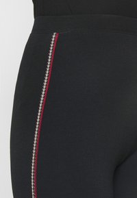 Zwarte leggings met een aansluitend ontwerp, met een contrasterende rode en crèmekleurige zigzag zijstrook. Gemaakt van een gladde, rekbare stof.