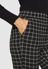 Black and white checkered pants with a tailored fit, featuring a side pocket and smooth texture, paired with a ribbed black sleeve.