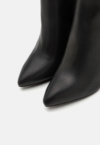 Paire de bottes en cuir noir à bout pointu vues de face sur un fond clair.