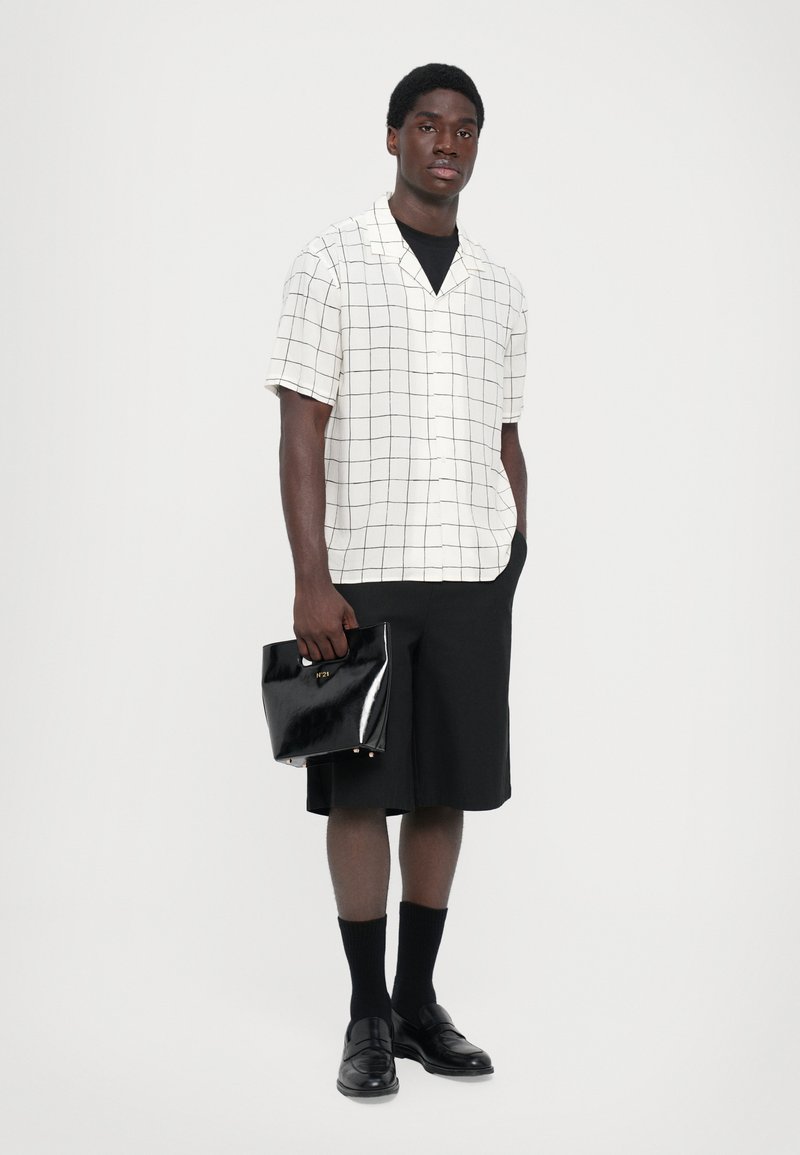 Kortärmad rutigt skjorta i vitt och svart, kombinerad med svarta shorts. Håller en blank svart väska med guldaccent. Svarta loafers och strumpor.