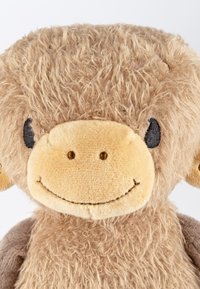 Plush toy monkey with soft, fuzzy beige fur. Round face features a light tan snout, embroidered eyes, and a smiling mouth.