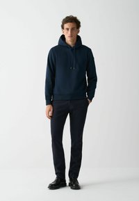 Hanorac bleumarin cu șnur, manșete și tiv cu elastic; combinat cu pantaloni închiși la culoare și încălțăminte neagră; textură de țesătură netedă.