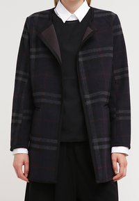 Marineblauer und grauer karierten Mantel mit strukturiertem Design, breitem Kragen und kontrastierender schwarzer Einfassung. Weicher, texturierter Stoff mit Taschen.