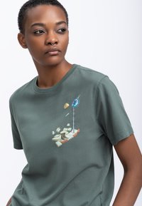 Groene katoenen t-shirt met een kleurrijke, grafische print waarop een scène is afgebeeld met elementen zoals een straatnaambord, gebroken stoep en verschillende voorwerpen.