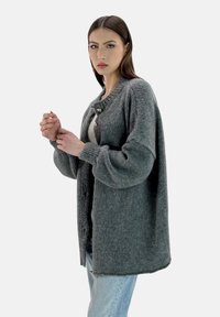 Cardigan grigio a maglia con una vestibilità morbida, presenta un colletto rotondo, maniche lunghe e due bottoni sul davanti per la chiusura.