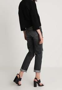 Pull noir court à manches trois-quarts, associé à un jean en denim foncé taille haute déchiré et des sandales à talons noires.