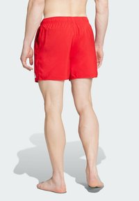 Červené plavky s elastickým pásom, krátka dĺžka, hladká textúra a bočné vrecká. Tkanina vyzerá ľahko a rýchloschnúca.