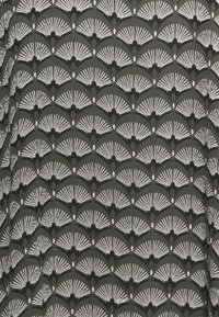 Tissu vert avec un motif de fans en blanc et noir. Le design présente des formes courbes alternées et de petits détails en forme de cœur.