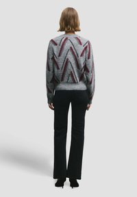 Hall halli burgundi ja musta ziczac-mustriga džemper, kitsad varrukaäärised ja ümar kaelus, kombineeritud lõdva mustade lehvidega teksadega.