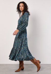 Dlouhé modré šaty s vzorem paisley, dlouhými rukávy, výstřihem do V a patrovým, volánkovým lemem. V kombinaci s hnědými kotníkovými botami.