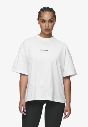 Weißes, übergroßes T-Shirt aus Baumwolle mit rundem Halsausschnitt und kurzen Ärmeln. Auf der Vorderseite steht der Text "PEGADOR" in Schwarz.