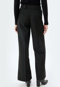 Zwarte pinstripe wijde pijpen broek van gestructureerde stof, met een op maat gemaakte tailleband en persvouwen voor een gestructureerde uitstraling.