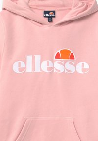 Felpa rosa con tasca frontale, caratterizzata da un grande logo bianco "ellesse" e una grafica solare colorata sopra il testo. Materiale in cotone morbido.