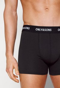 Schwarze Boxershorts mit einem breiten elastischen Bund, auf dem "ONLY&SONS" in Weiß geschrieben steht. Aus glattem Stoff und mit einer eng anliegenden Passform.