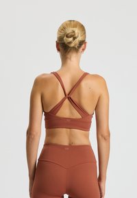 Mauve Sport-BH mit kreuzgefertigten Trägern und glatter Textur. Begleitet von passenden, hoch geschnittenen Leggings, beide aus dehnbarem Material gefertigt.
