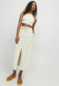 Top de halter corto color crema combinado con una falda de cintura alta y largo hasta el tobillo, con una abertura frontal y cintura con cordón. Chanclas amarillas.