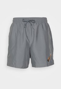 Shorts de sport gris avec ceinture élastique et cordon, avec un petit logo orange et noir près de l'ourlet inférieur droit.