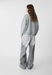 Grauer, gestrickter Pullover mit lockerer Passform, kombiniert mit hellgrauen, acid-wash, weit geschnittenen Jeans mit Gesäßtaschen und fransigen Säumen.
