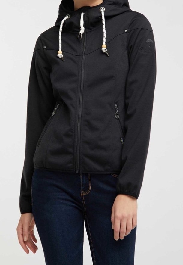 Chaqueta negra con cremallera y capucha, que presenta una textura suave, cordones ajustables y bolsillos laterales, combinada con jeans oscuros.