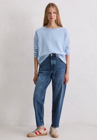 Hellblauer Pullover mit lockerer Passform, kombiniert mit hoch taillierten dunkelblauen Jeans und beigen Sneakers mit roten Akzenten.