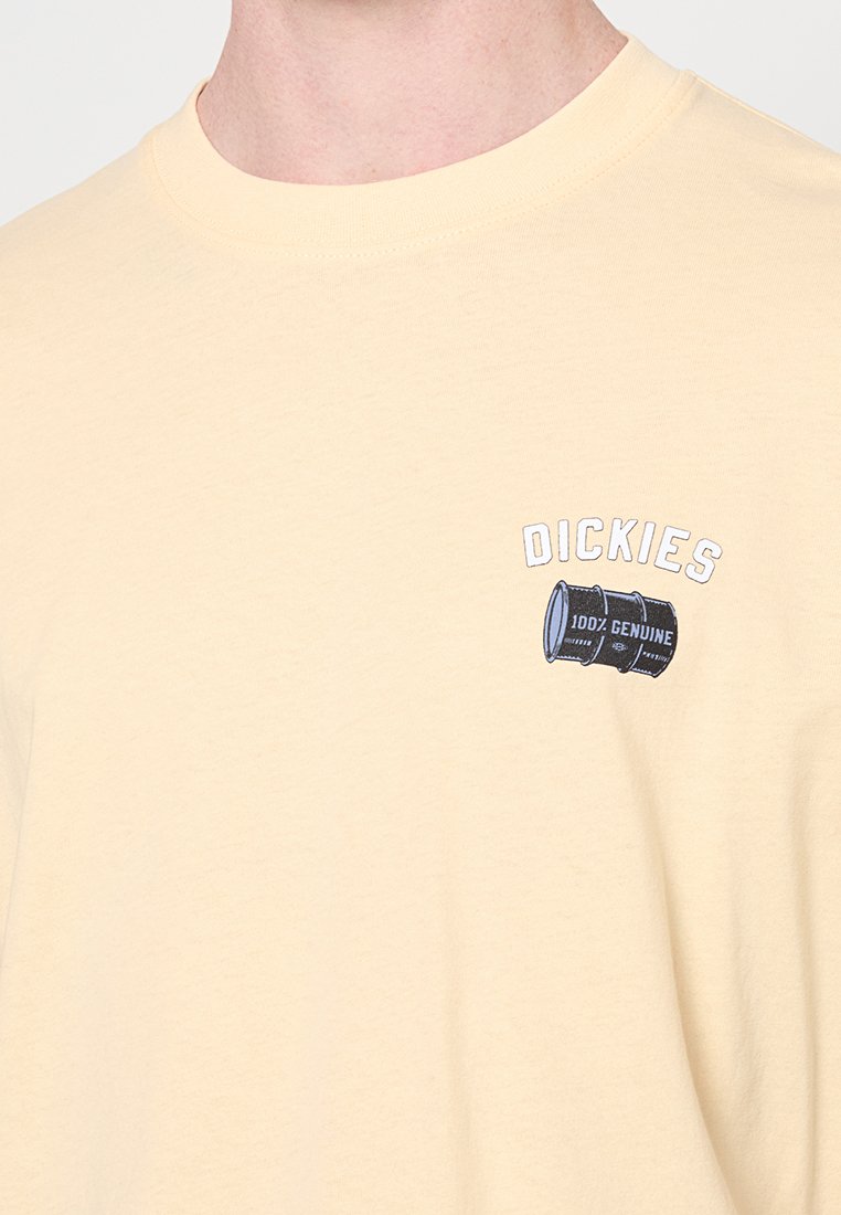 T-shirt beige con una piccola grafica di una botte nera e testo "DICKIES 100% GENUINE" sul petto sinistro.