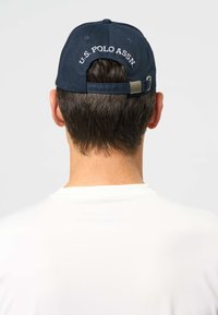 Șapcă de baseball bleumarin cu logo-ul brodat „U.S. POLO ASSN.” pe partea din spate, prevăzută cu o curea reglabilă și textură moale a materialului.
