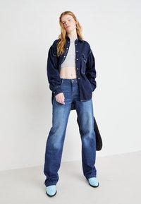 Mørkeblå denimjakke i oversized pasform med frontlommer; parret med lyseblå hæle mules og medium vaskede lige bukser.